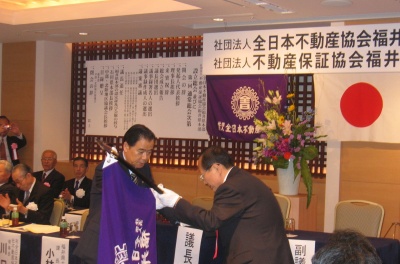 総本部・川口理事長(写真左)から協会旗を受け取る藤本本部長