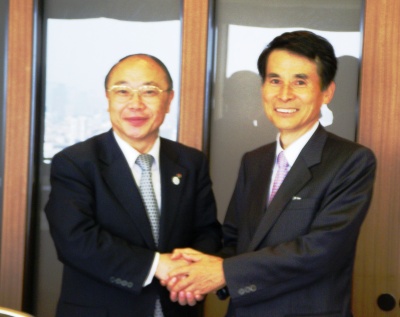 新理事長に就任する池田行雄氏(左)と握手を交わす、岩崎芳史理事長