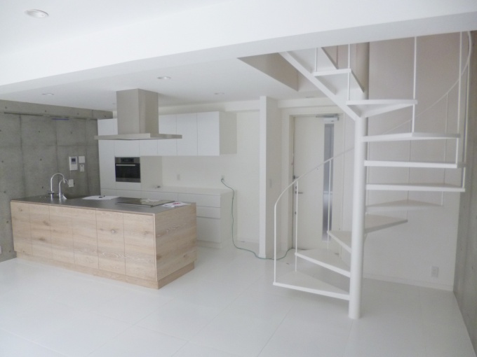 地階が1階になっているメゾネットタイプの部屋。壁はコンクリート打ちっぱなしで、白を基調としたシンプルな空間。キッチンはオーダーメイド