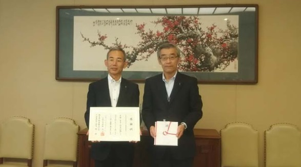 大阪市役所にて、感謝状を受け取る同社専務取締役の藤井 孝氏(左)