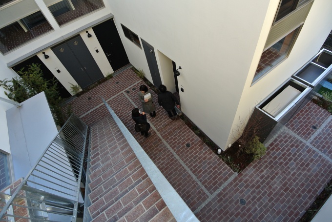2階のワンルーム玄関から中庭を見る。階段もレンガ貼り。メゾネット住戸のサンルーム窓からのぞくレンガ床と、中庭のレンガが連続した空間となっている